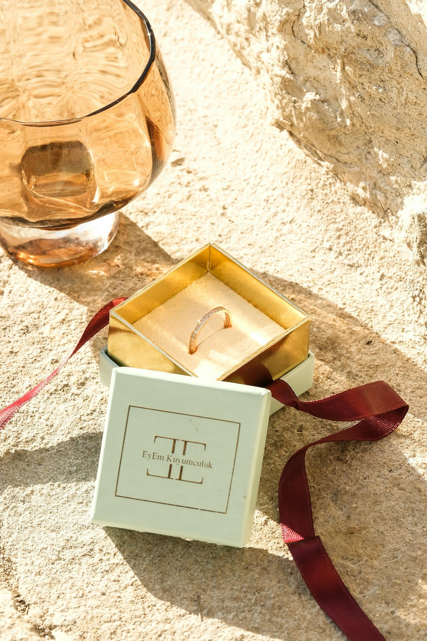 A minimalist gold ring displayed in an elegant jewelry box on a sunlit stone surface.