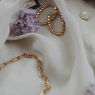 Stylish close-up of gold jewelry set against a light fabric with purple flowers, exuding elegance.
