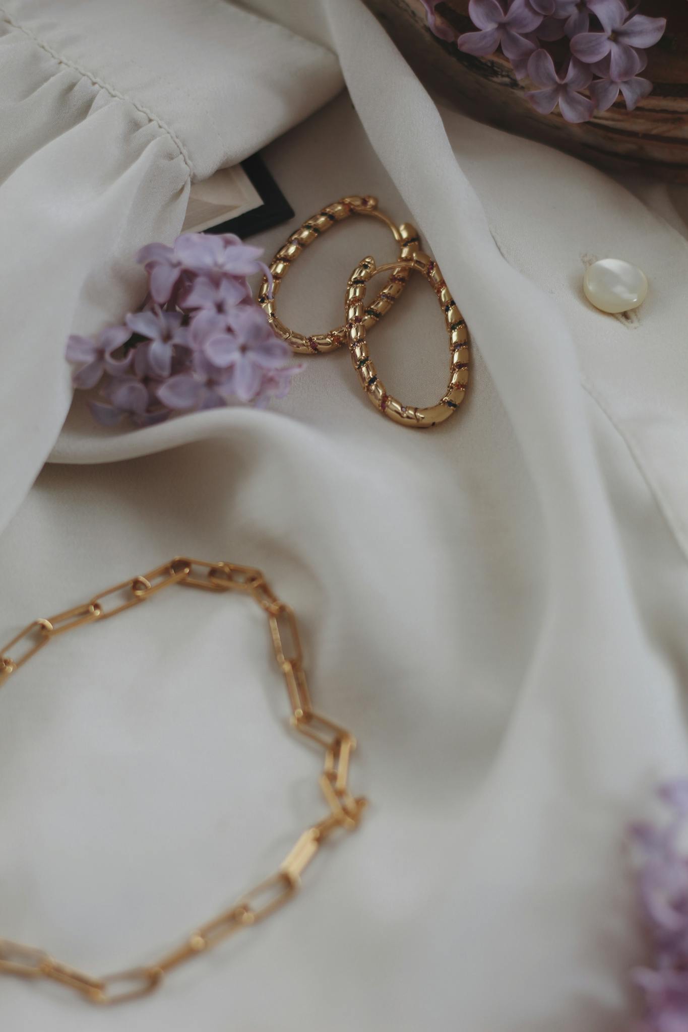 Stylish close-up of gold jewelry set against a light fabric with purple flowers, exuding elegance.