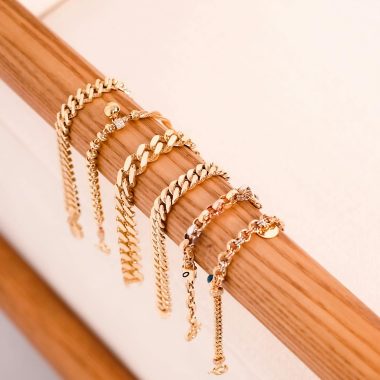 Stylish gold bracelets elegantly draped over a wooden rod, showcasing luxury and style.